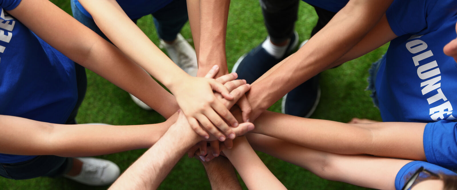 Group of volunteers in blue shirts with hands stacked together.