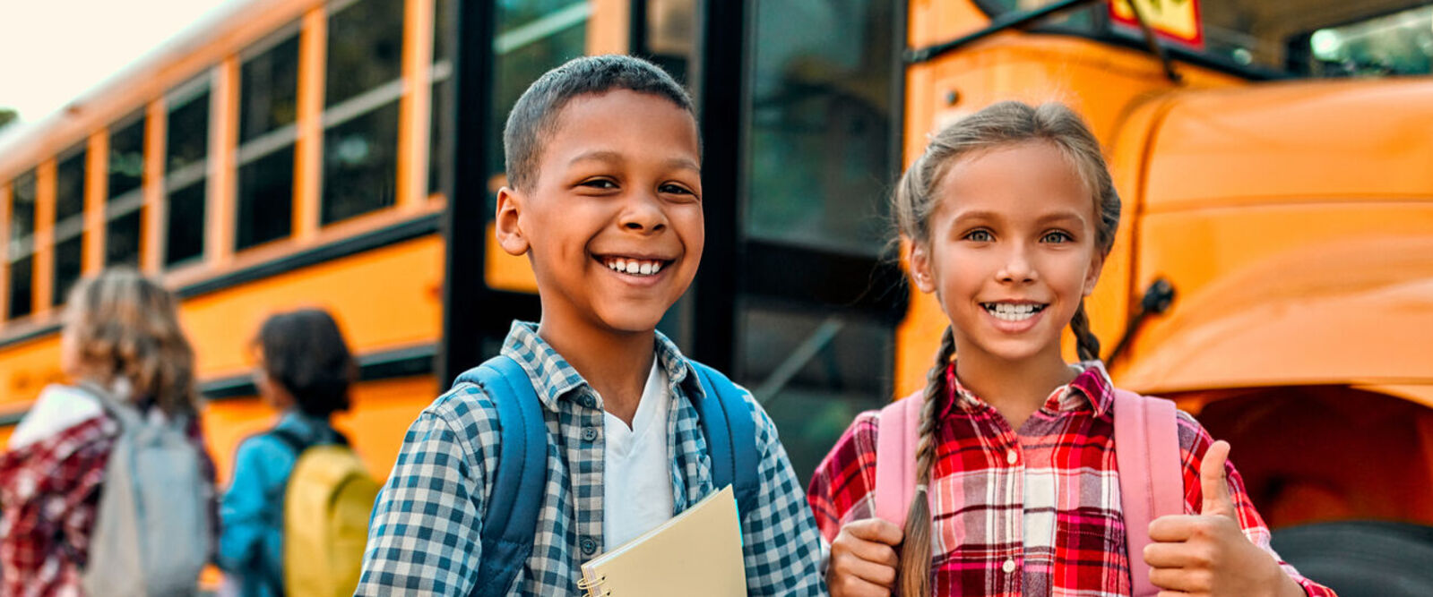 Smiling schoolchildren standing in front of a yellow school bus.